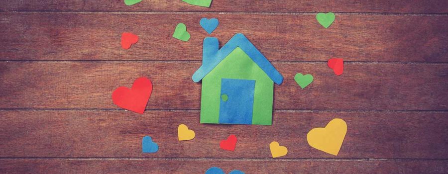 Ein buntes Haus aus Papier und bunte Herzen aus Papier liegen auf einem Holztisch | Valentinstag Immobilien Makler