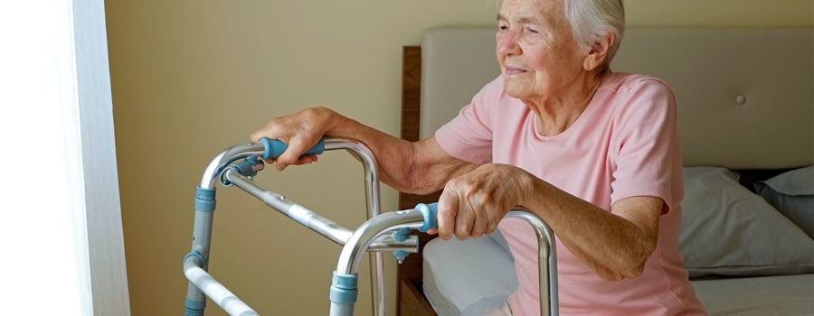 Seniorin sitzt auf einem Bett und hält sich am Rollator fest | Umzug ins Pflegeheim