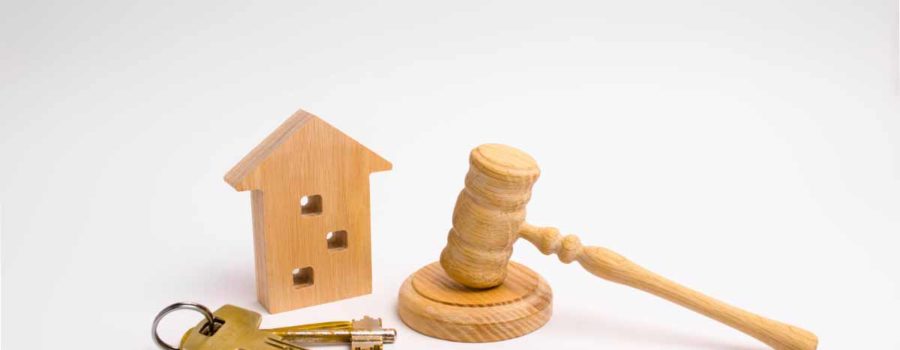 Ein Schlüsselbund, ein Häuschen aus Holz und ein Richterhammer liegen auf einer weißen Oberfläche - Immobilienverkauf